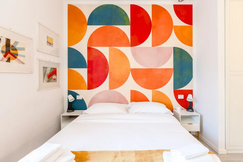 Comfortable bed against a colorful geometric mural wall in a stylish Townhomes Milano Mid-Century Modern apartment stay.