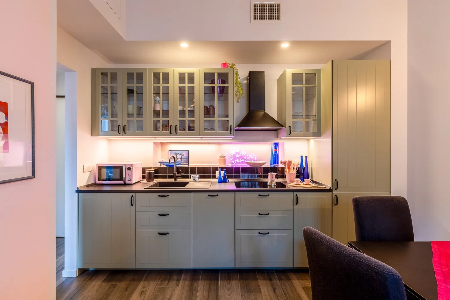 Modern kitchen with white cabinets, built-in oven, and soft ambient lighting in the Colorful Eclectic apartment by Townhomes Milano.