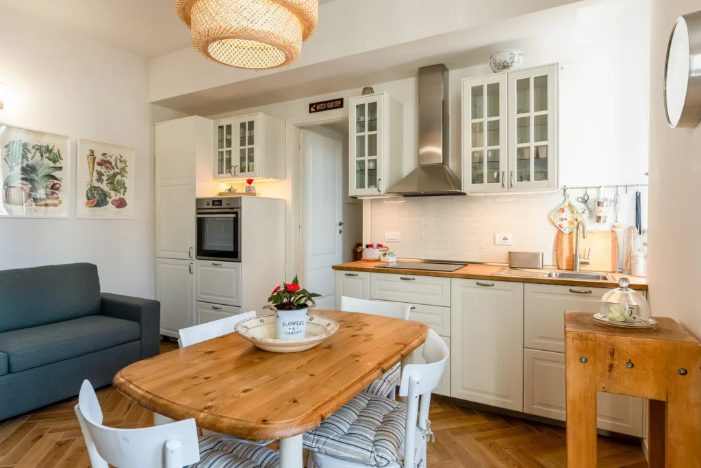 Bright kitchen with wooden dining table, pendant lighting, and white cabinets in Scandinavian Minimal Apartments by Townhomes Milano.