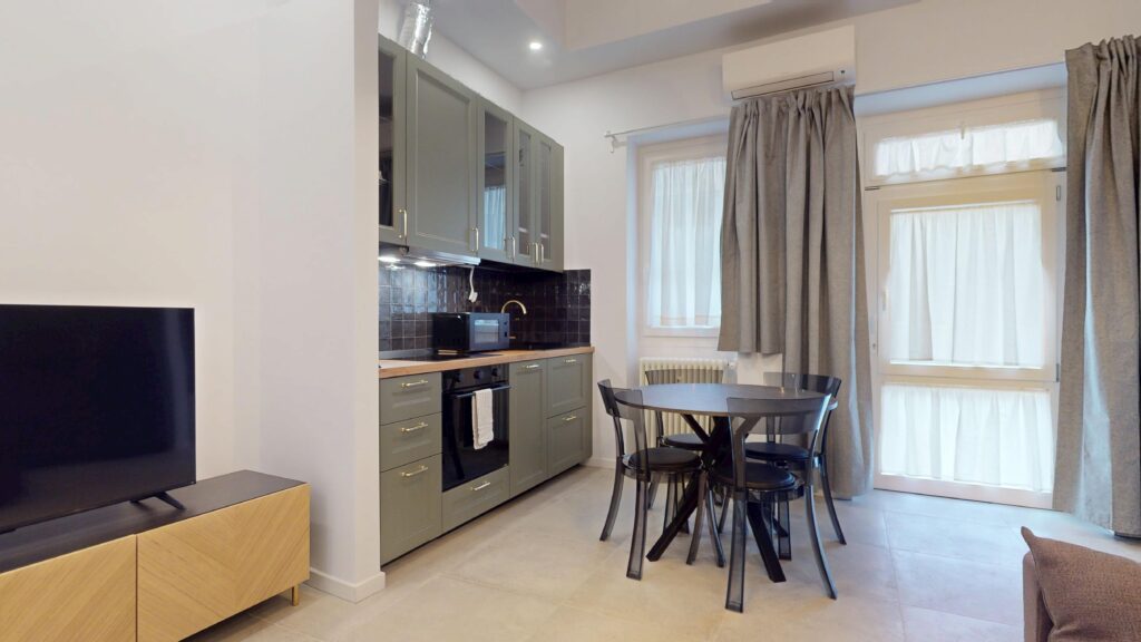 Modern rental apartment kitchen with sage-green cabinetry and a circular dining table, perfect for international tourists and travelers visiting Milan, Italy, with Townhomes Milano.