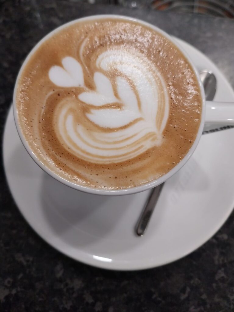 A close-up photo of a cup of coffee, likely a latte or cappuccino, on a white saucer.