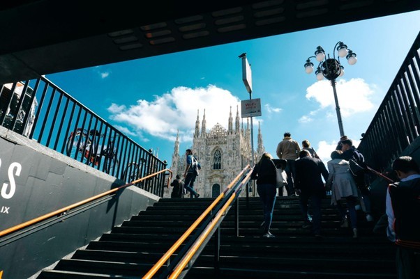 People walking up stairs toward the Milan Duomo cathedral under a blue sky, Milan city center.