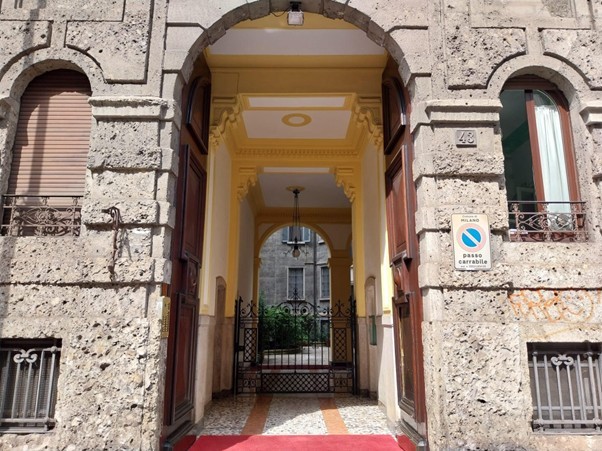 Stone arched entryway and red carpet leading into the Townhall Milano courtyard.