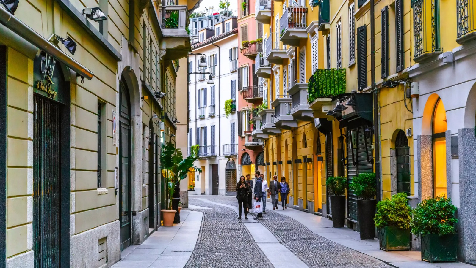 Vibrant Milan historic street with colorful buildings, cobblestone path, and green plants