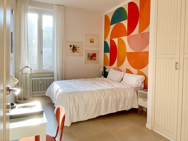 Bright modern bedroom with white bed, colorful geometric wall art, and natural light