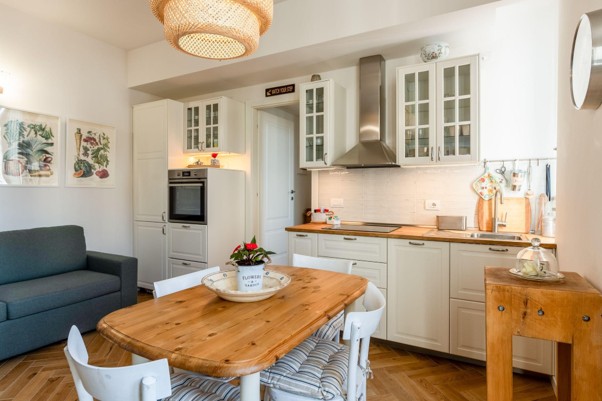 Bright open-plan kitchen and living area with cream cabinets, wooden table, and teal sofa