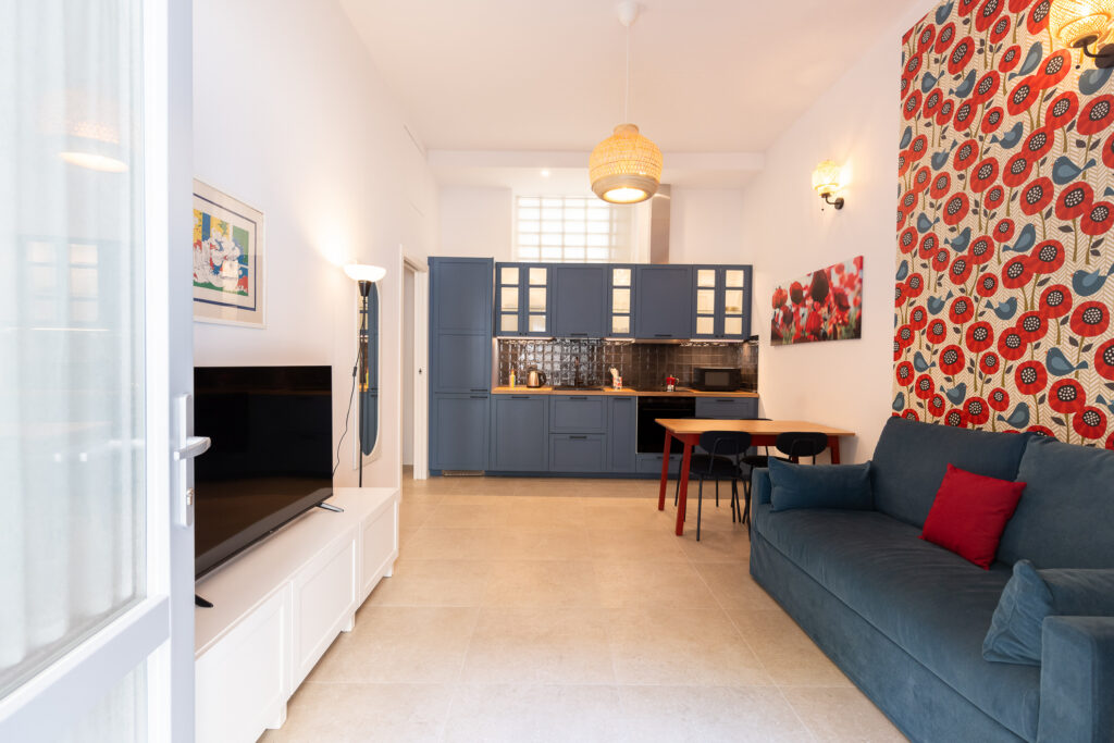 Contemporary studio with navy kitchen, blue sofa with red accents, and bold geometric curtain